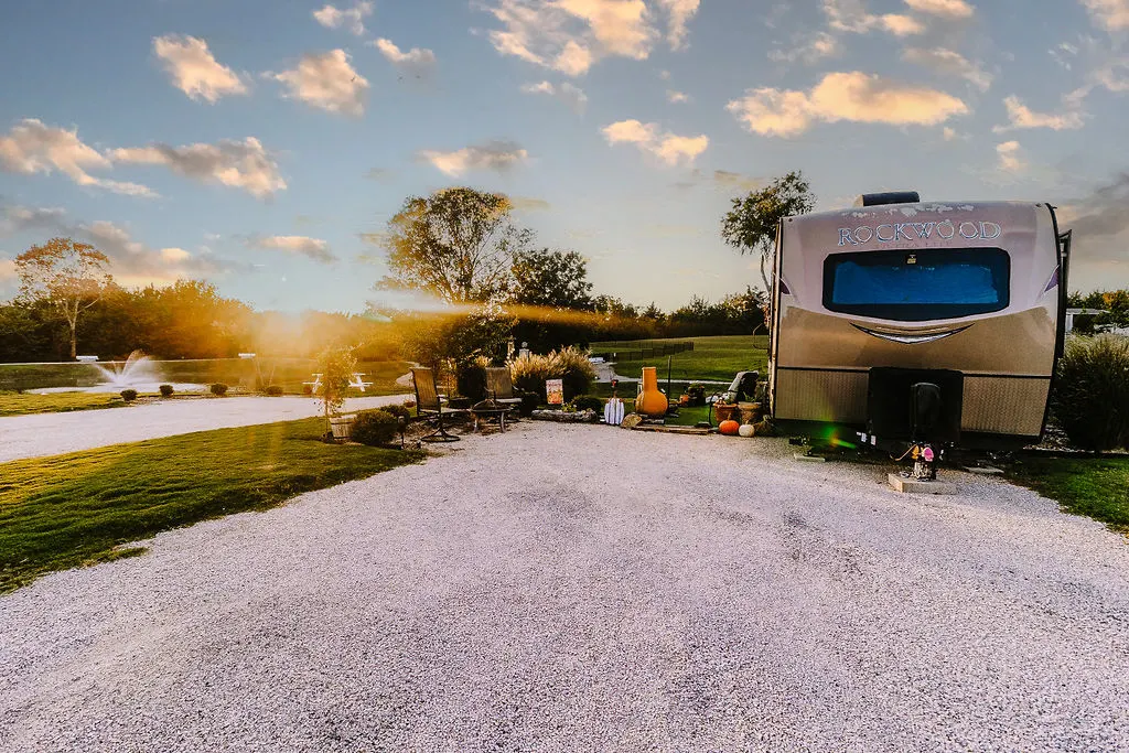 Landscaped RV site patio with Adirondack chairs and mature trees at sunset